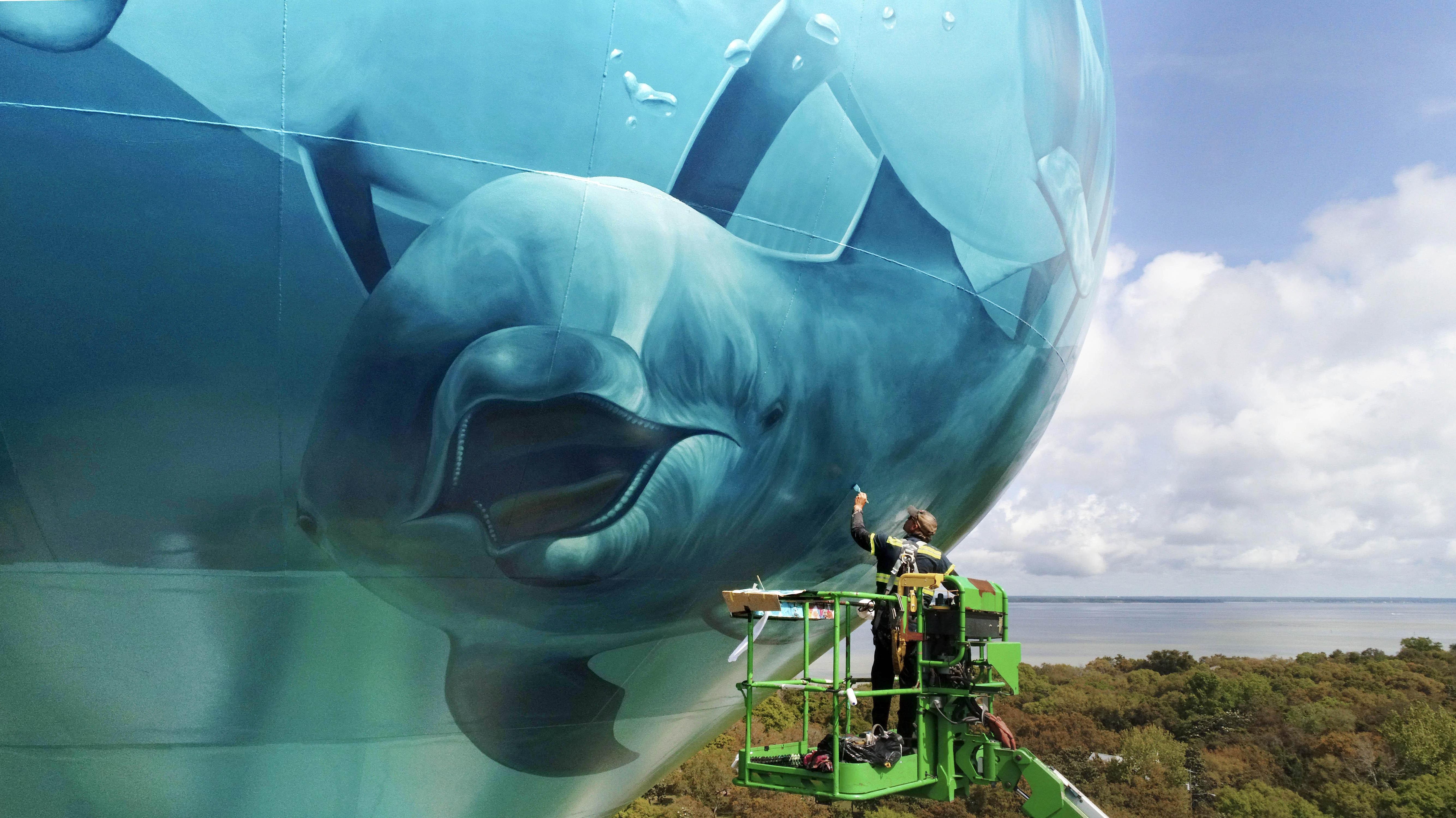 Artist Eric Henn uses rollers and paint brushes to paint a series of sea life murals on the new water tower off of Calhoun Avenue in Destin earlier this week. In addition to the dolphins, the tower also features a sea turtle and will have a coral reef around the base when Henn is completed.
